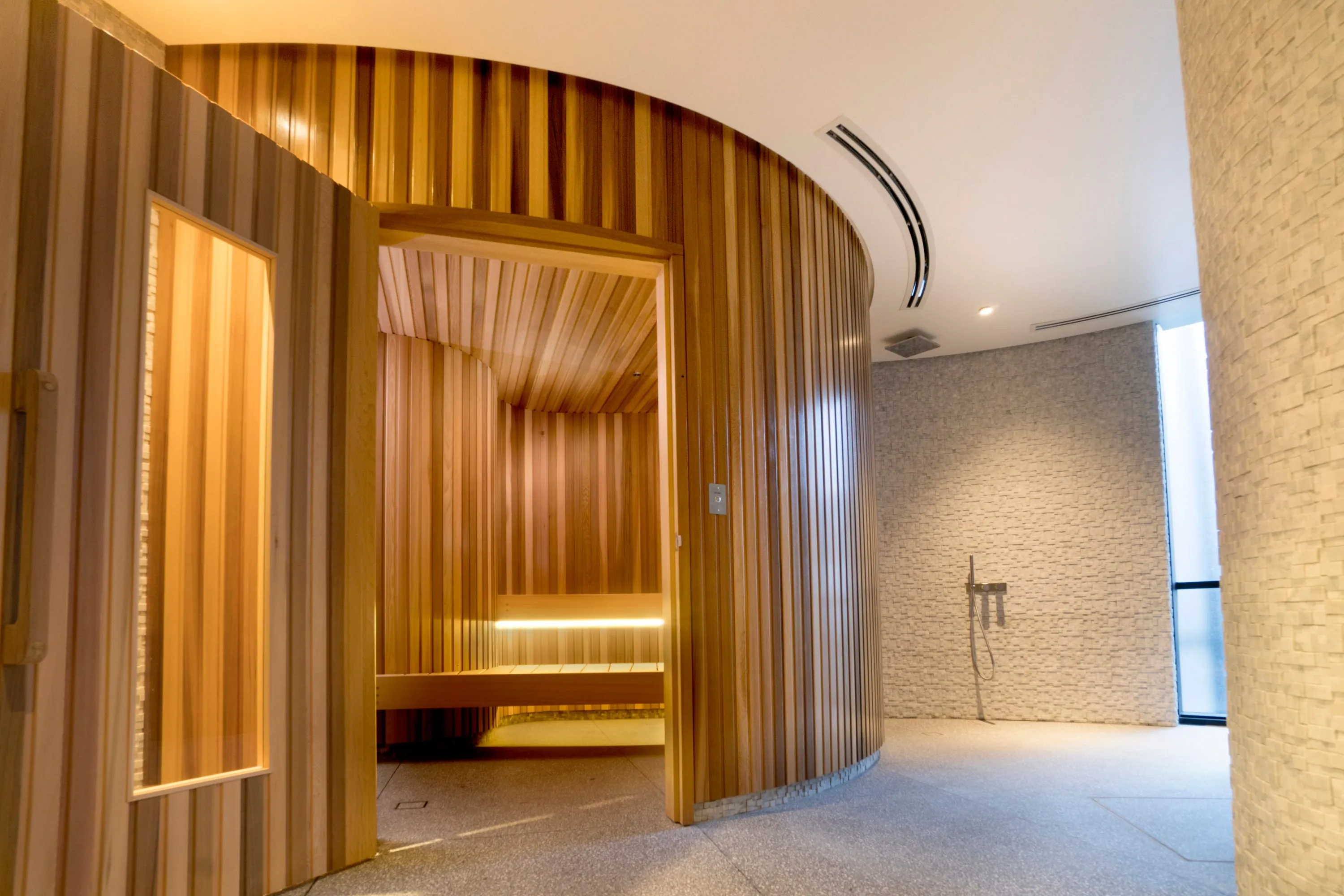 Looking into a curved cedar sauna with softly lit tiered benches