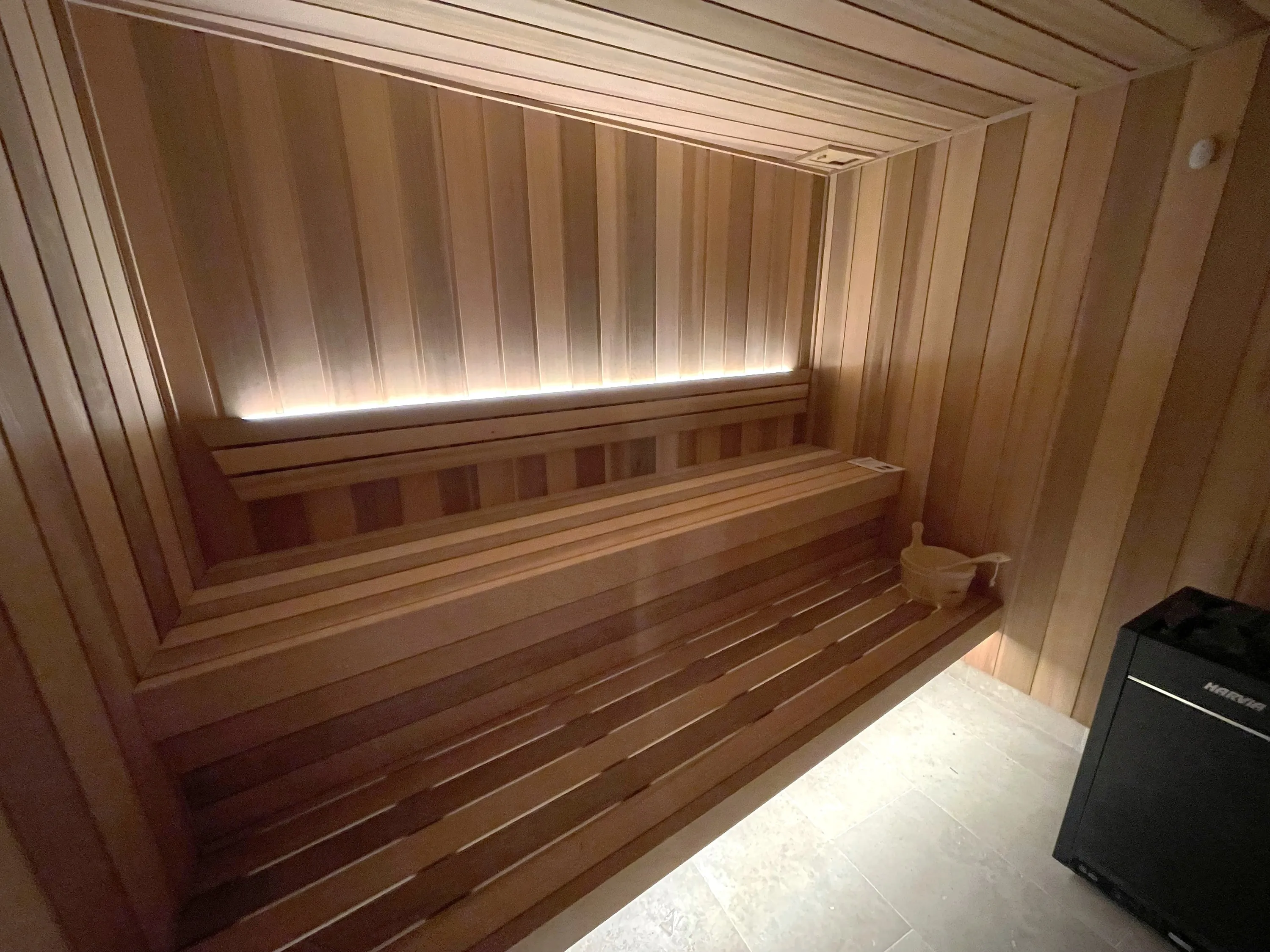 Timber home sauna with long benches, a concealed light line and a floor-standing heater